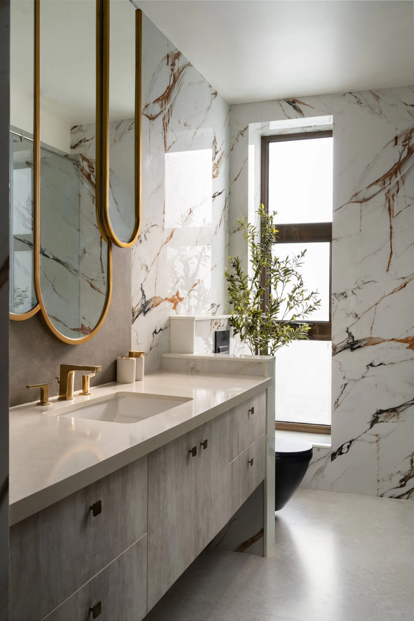 Bathroom with veined marble walls and arched gold mirrors