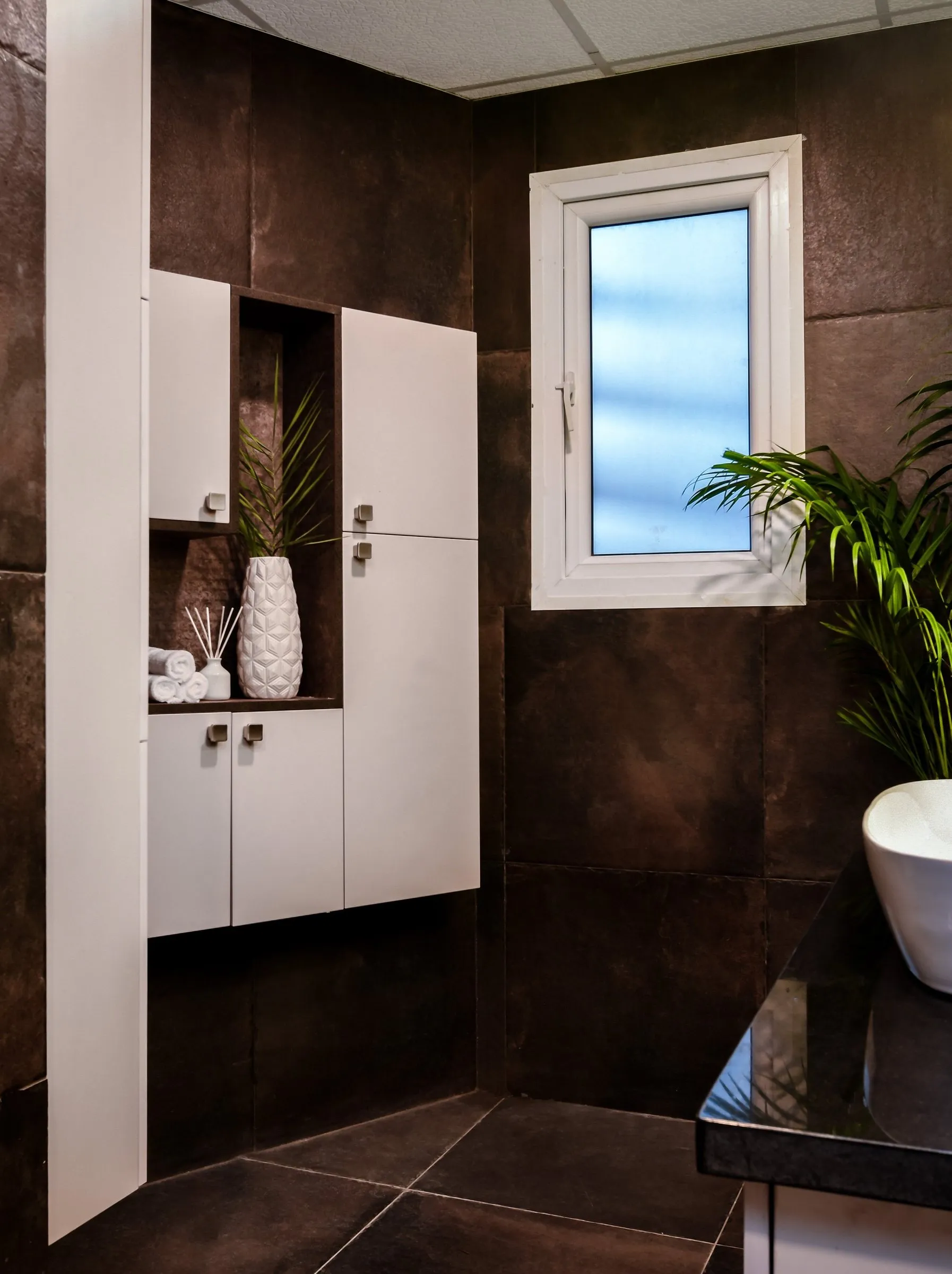 Bathroom with dark tiles and a tall white storage unit