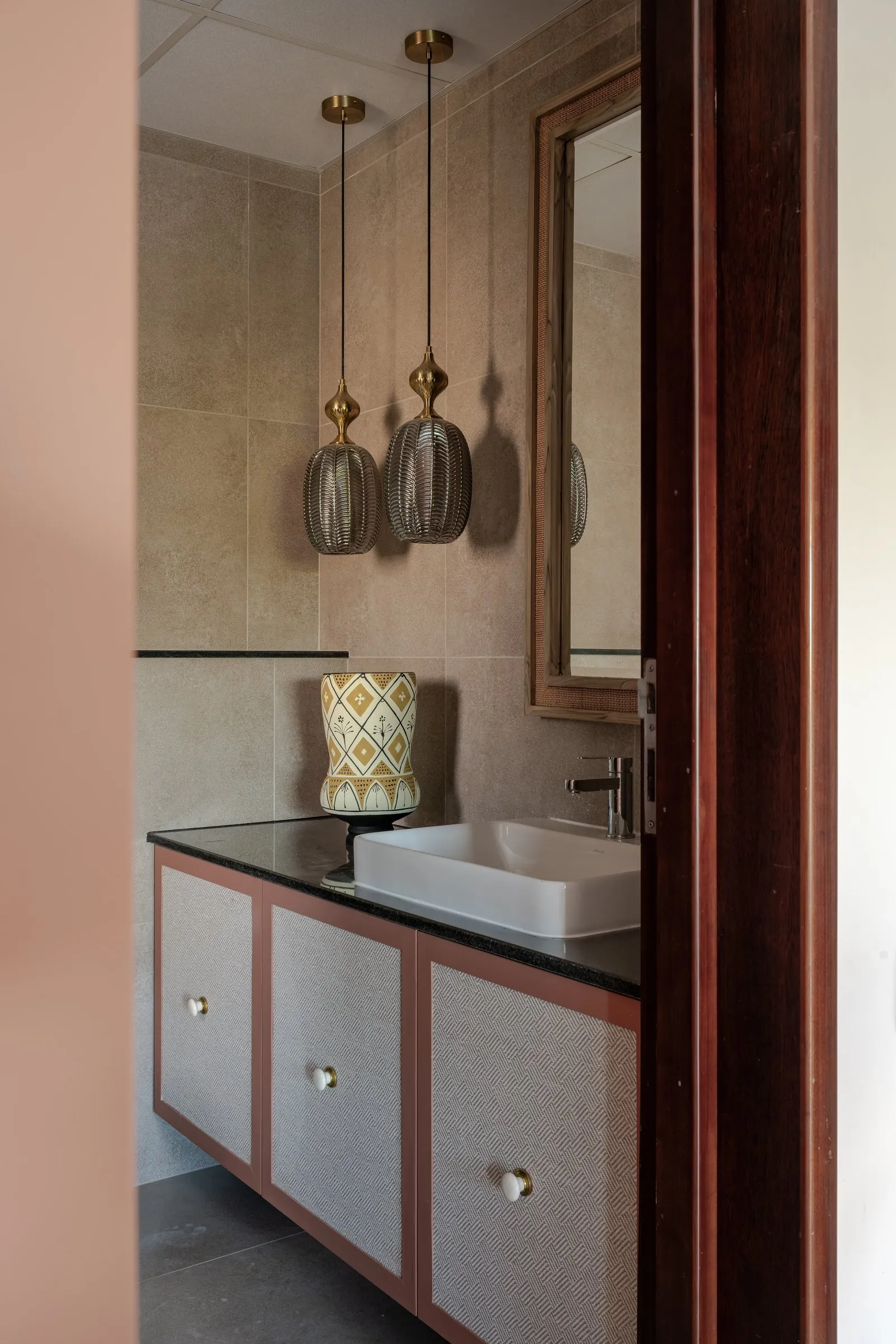 Blush vanity with a stone basin and ribbed glass pendants
