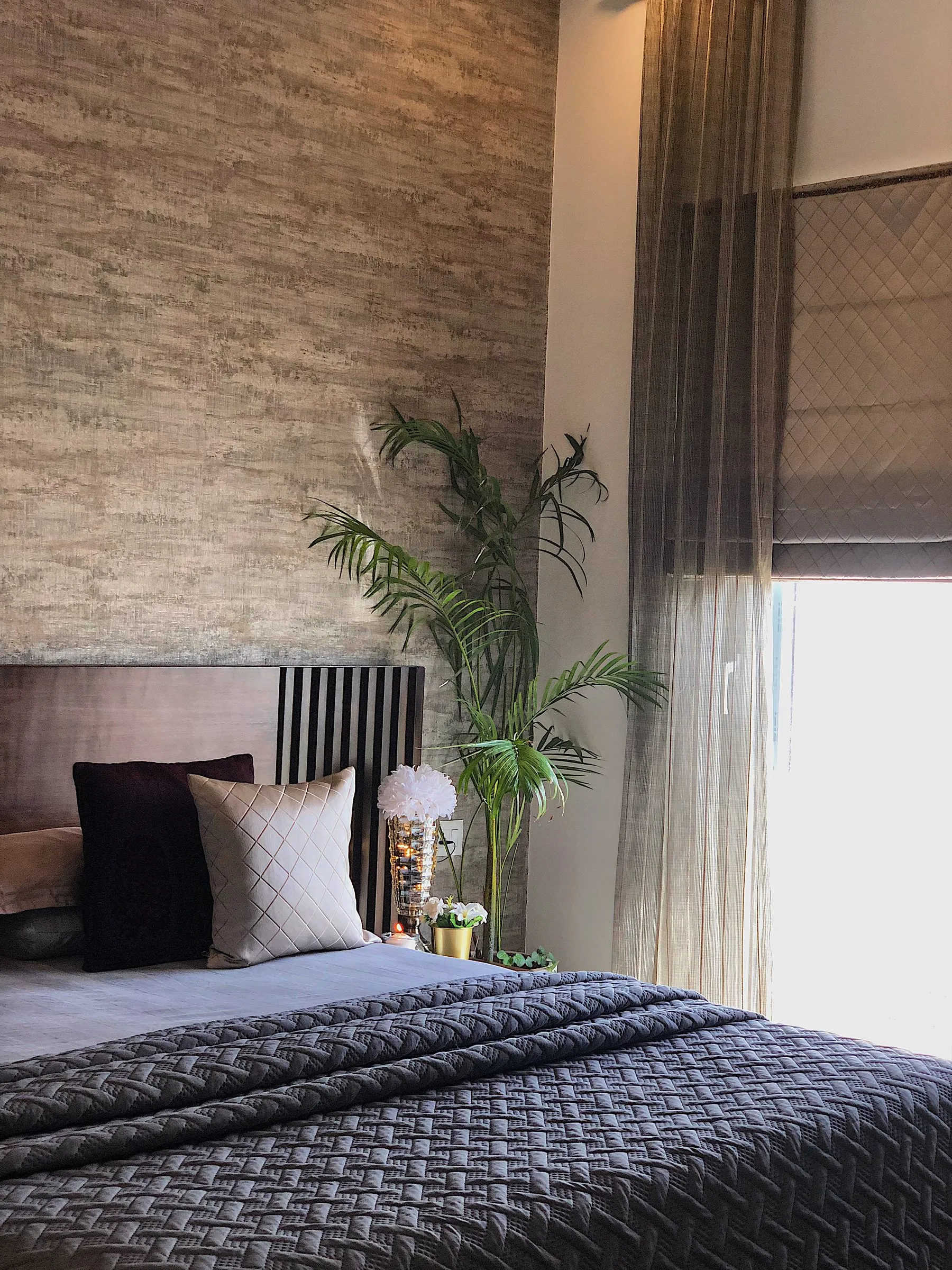 Bedroom with a quilted dark bedspread and a textured wall