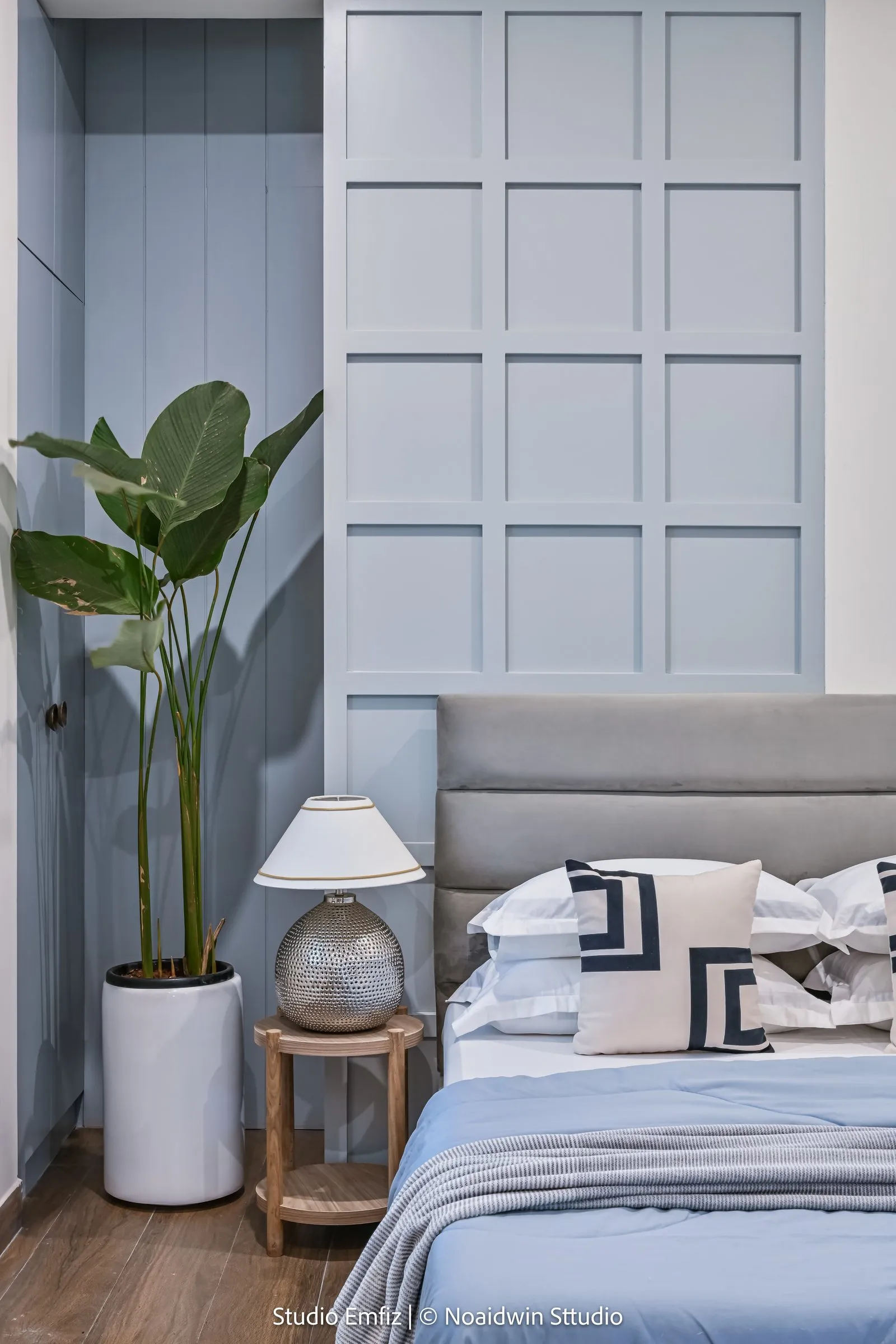 Blue bedroom with a grey headboard and a tall plant