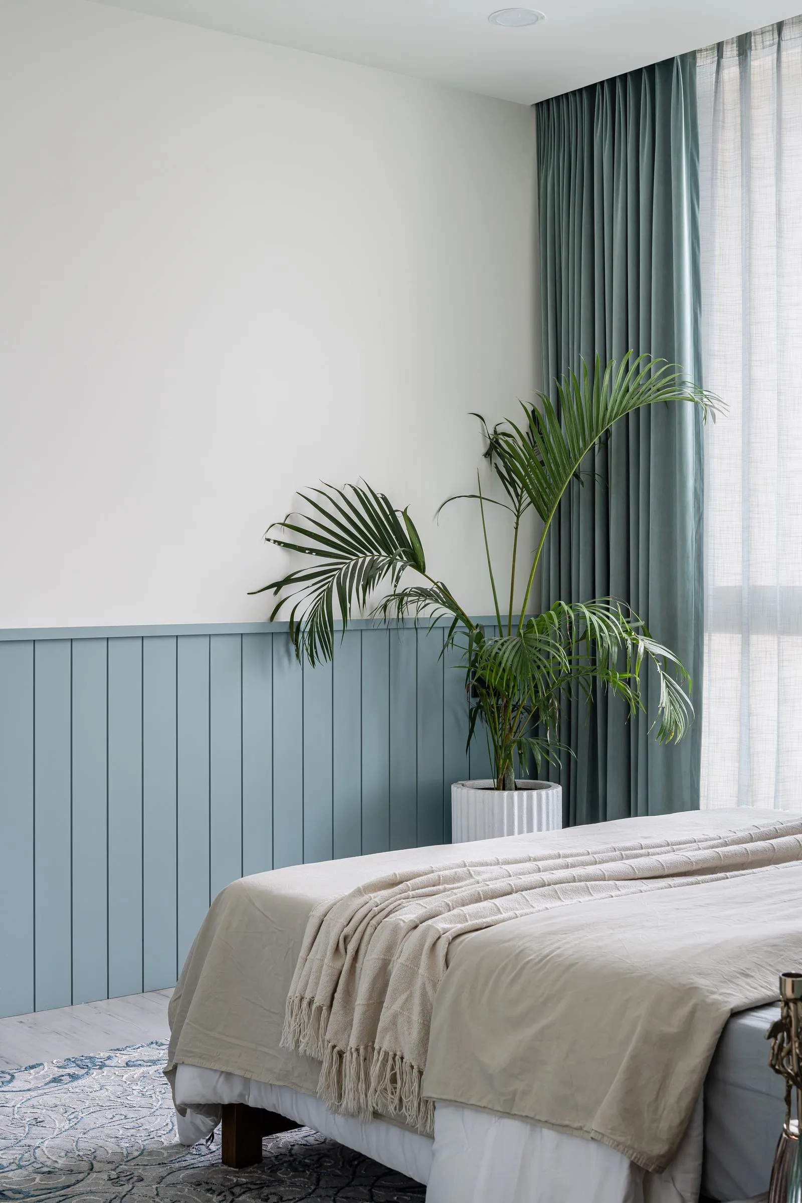 Bed by a window with teal curtains and a palm