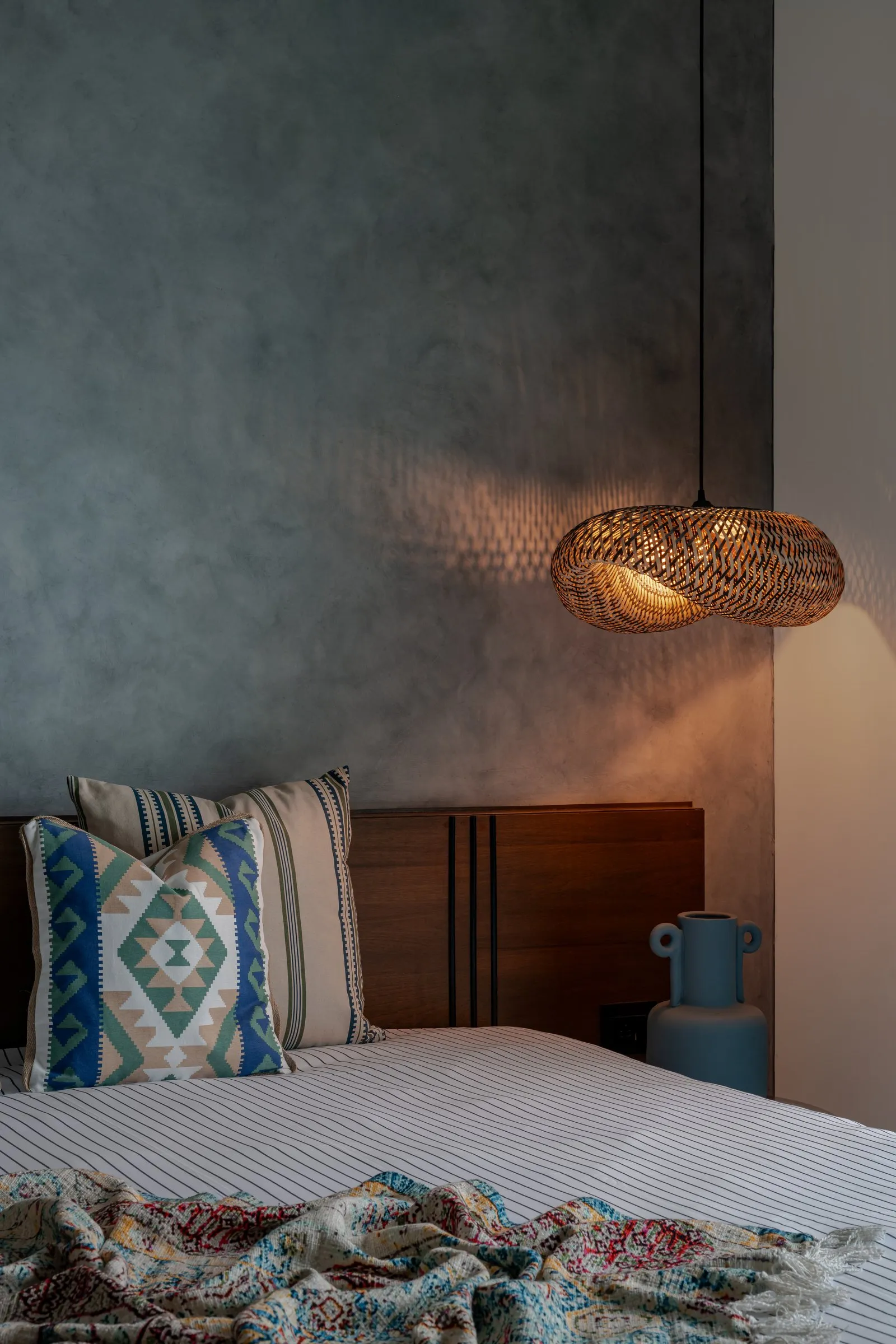 Bedroom with a grey limewash wall and a woven pendant light