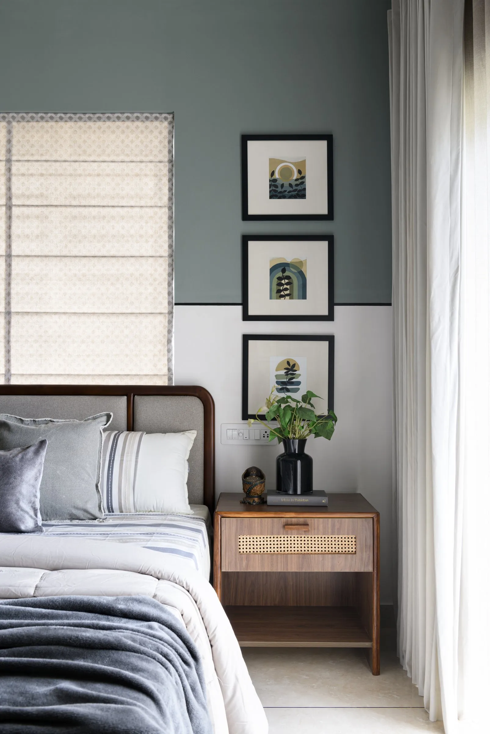 Sage bedroom with framed prints and a rattan bedside table
