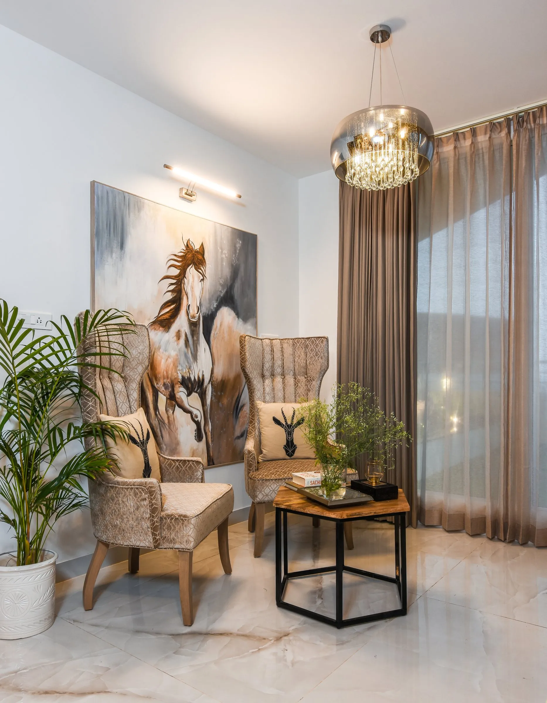 Two velvet wingback chairs beneath a horse painting and a smoked glass chandelier