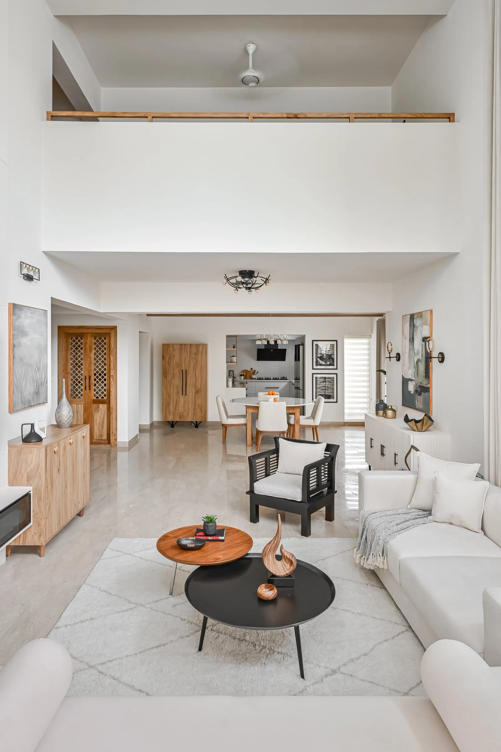 Double-height living room with white sofas, round coffee tables and tall sheer curtains