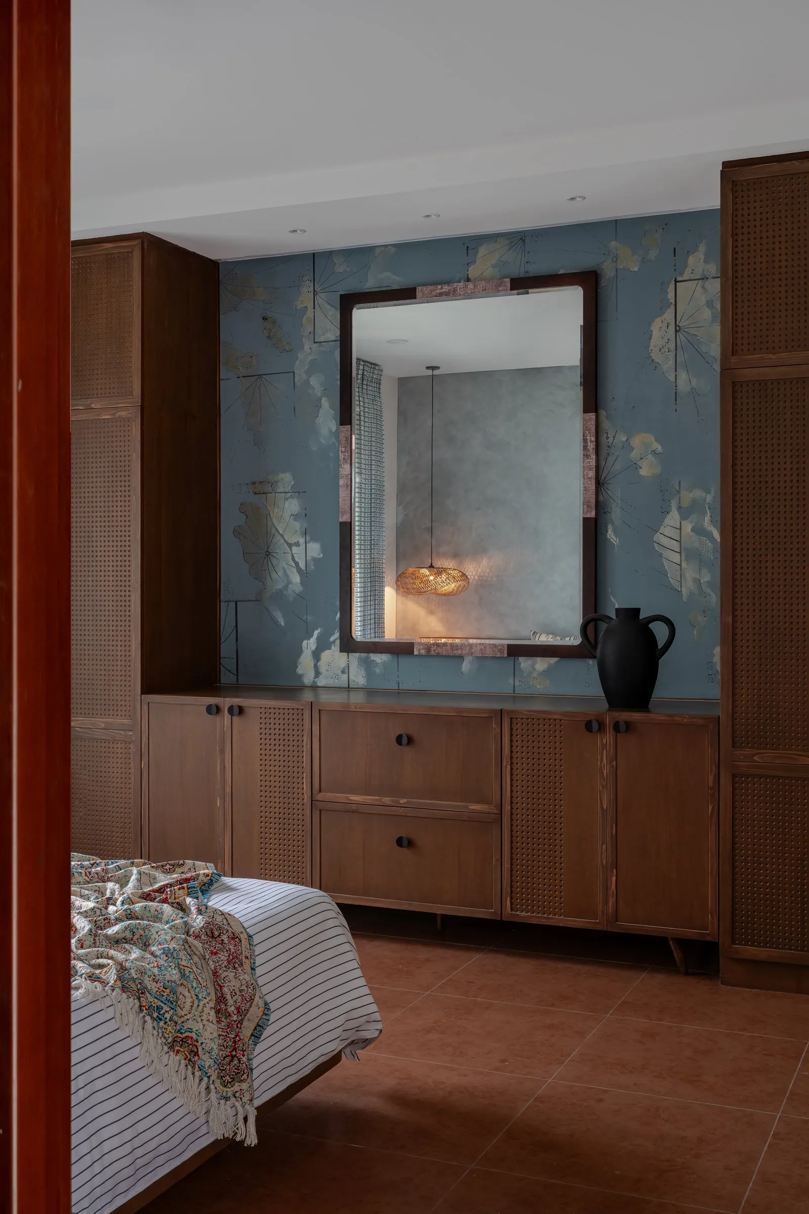 Teak cabinet under a mirror on a blue botanical wall