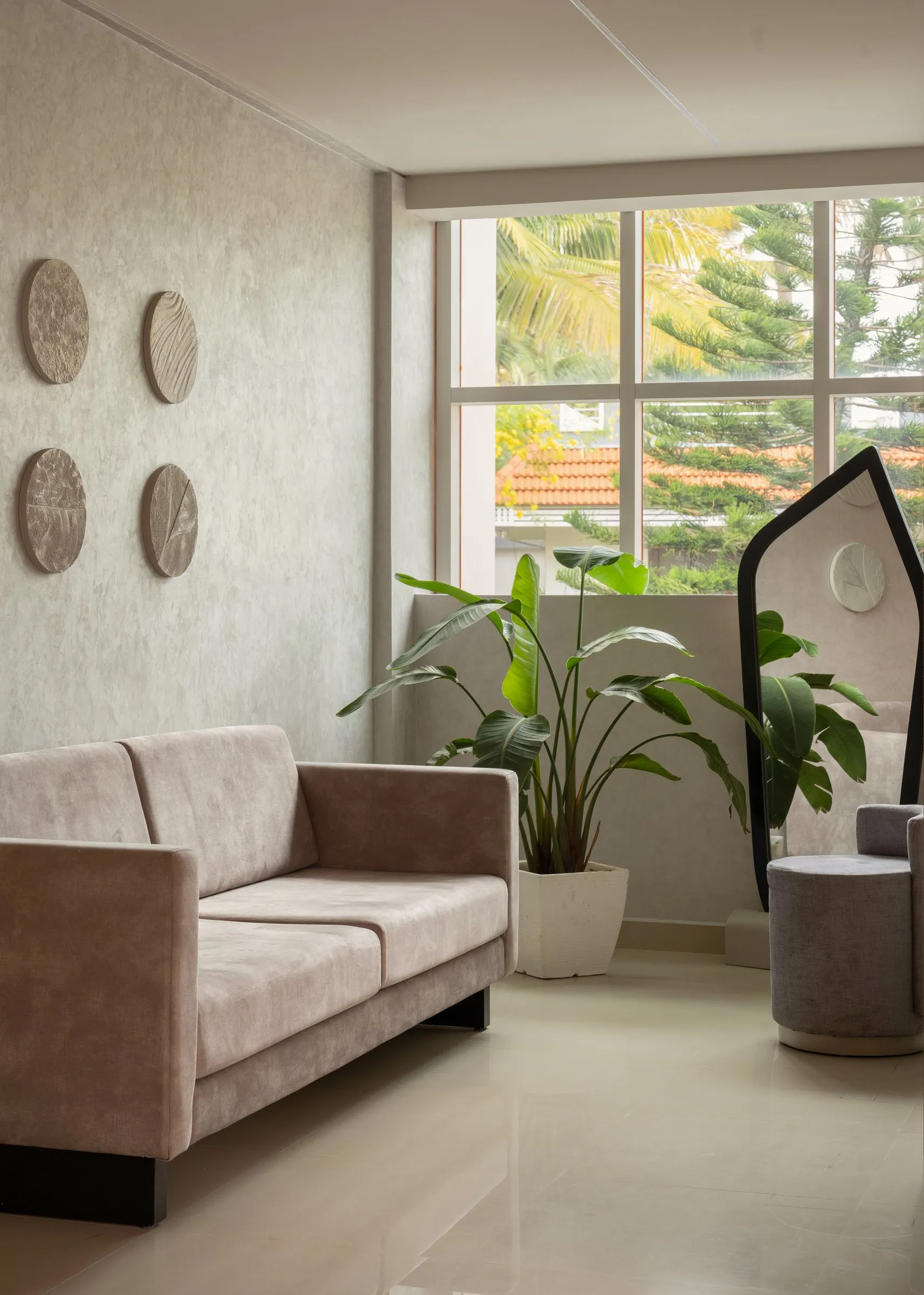 Blush sofa by a large window with round wall pieces and a plant