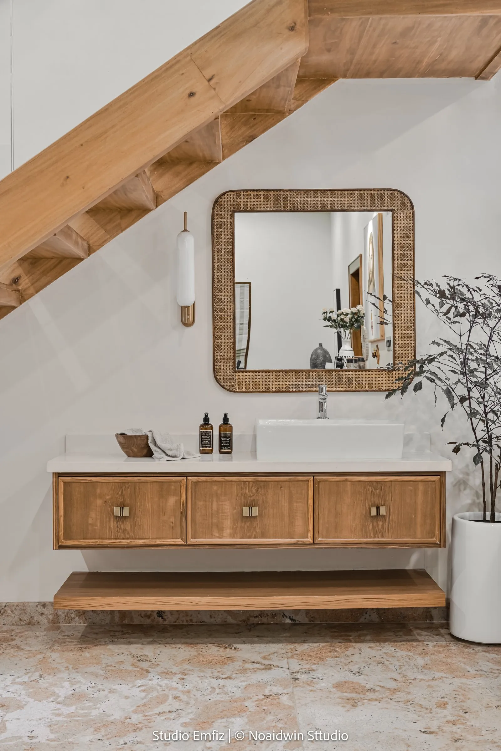 Floating oak vanity with a cane mirror under the stairs