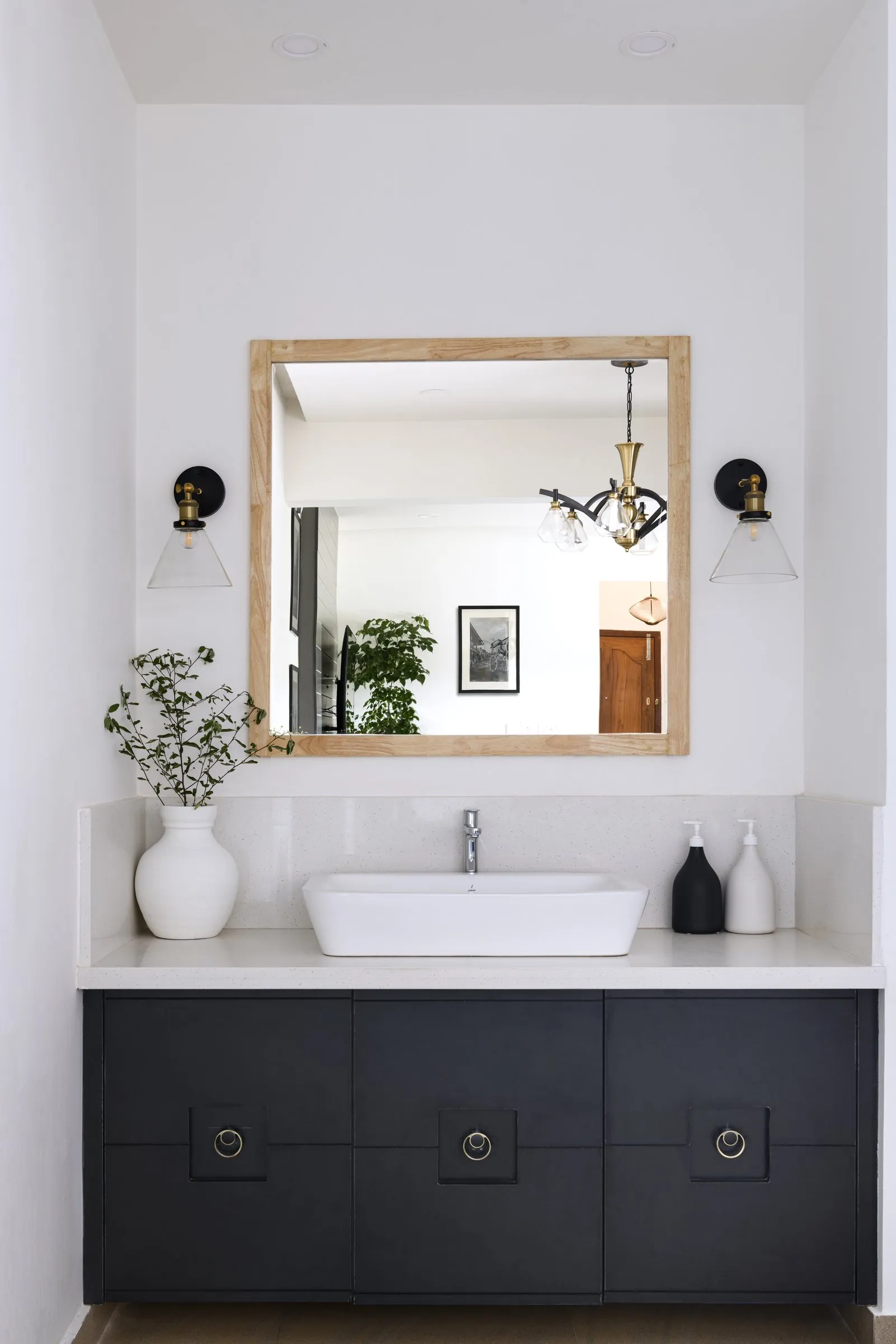 White basin on a black cabinet with an oak-framed mirror and wall lights